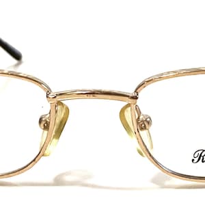 May include: Gold-tone metal eyeglasses with clear lenses. The brand name "Roberto Elliot" is printed on the right lens.