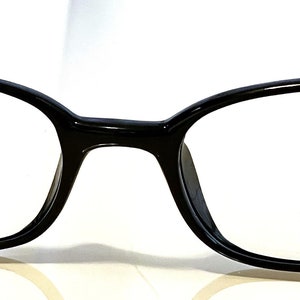 K&ouml;nnte beinhalten: Schwarze, ovale Brille mit klaren Gl&auml;sern. Die Fassungen sind gl&auml;nzend und haben eine leichte Kr&uuml;mmung an der Oberseite. Das Wort "Max" ist kursiv auf dem rechten Glas geschrieben. Klassisches Design.