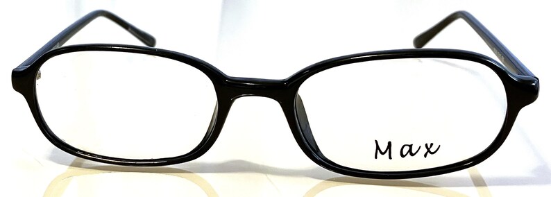 K&ouml;nnte beinhalten: Schwarze, ovale Brille mit klaren Gl&auml;sern. Die Fassungen sind gl&auml;nzend und haben eine leichte Kr&uuml;mmung an der Oberseite. Das Wort "Max" ist kursiv auf dem rechten Glas geschrieben. Klassisches Design.