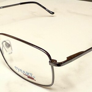 May include: A pair of rectangular eyeglasses with a dark brown frame. The lenses are clear, and the temples are thin and extend to the ear. The brand name "eyeART" is visible on the lens.