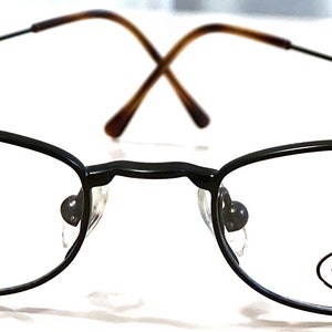 Könnte beinhalten: Schwarze Metallgestellbrille mit ovalen Gläsern. Der Markenname "STEVE MADDEN" ist auf dem rechten Glas aufgedruckt.