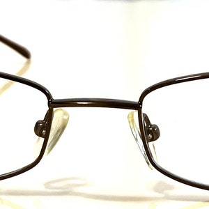 Könnte beinhalten: Braune Metallgestellbrille mit klaren Gläsern. Der Markenname "ROSSINI" ist auf dem rechten Glas aufgedruckt.