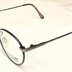 May include: A pair of eyeglasses with a dark frame and oval lenses. The temples are thin and extend to curved ear pieces. The nose pads are a light beige color. The text on the lens reads "Kenneth Cole New York".
