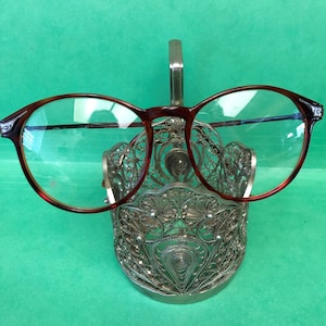 Puede incluir: Un portagafas de filigrana plateado con un par de gafas de montura marrón apoyadas en la parte superior.