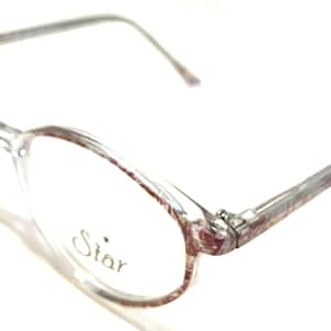 Könnte beinhalten: Transparente Brille mit einem rosafarbenen und weißen gemusterten Rahmen. Der Rahmen hat das Wort "Star" auf der Seite aufgedruckt.