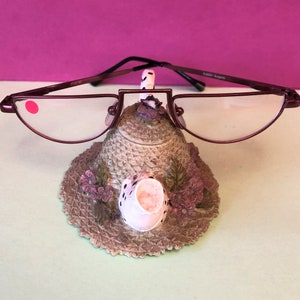 Puede incluir: Un portagafas de metal burdeos con forma de tetera con un diseño floral y un pico de tetera blanco. El portagafas está sobre una superficie verde claro.