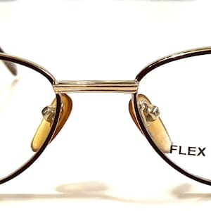 Può includere: Occhiali ovali in metallo dorato con montature marroni. Le montature hanno il testo "FLEX COLLECTION # 44" stampato sulla lente destra.