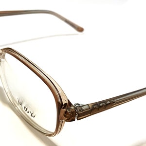 Może przedstawiać: Okulary z brązowego plastiku w kwadratowej oprawie. Okulary mają przezroczyste szkła, a na prawym szkle nadrukowano nazwę marki "Mavi".