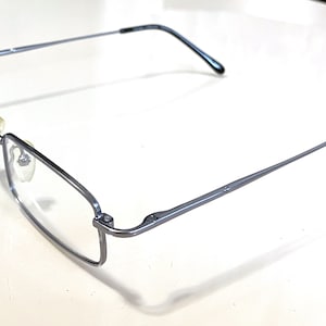 Könnte beinhalten: Silberfarbene Metallbrille mit klaren Gläsern und schwarzen Bügeln.