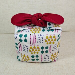 May include: A white fabric gift bag with a red ribbon tied around it. The bag has a colorful pattern of green leaves, pink and yellow flowers, and white dots.