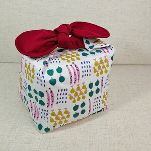 May include: A white fabric gift bag with a red bow. The bag has a pattern of green leaves, pink and yellow pears, and pink and white stripes.