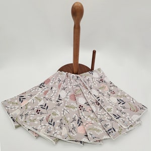 May include: A set of eight gray and white dishcloths with a floral pattern. The cloths are folded and displayed on a wooden countertop stand.