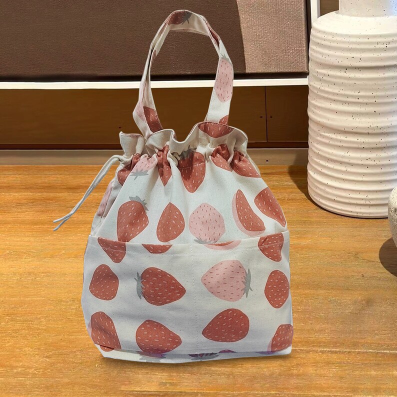 May include: A white drawstring bag with a pink and red strawberry print. The bag has two handles and a drawstring closure.