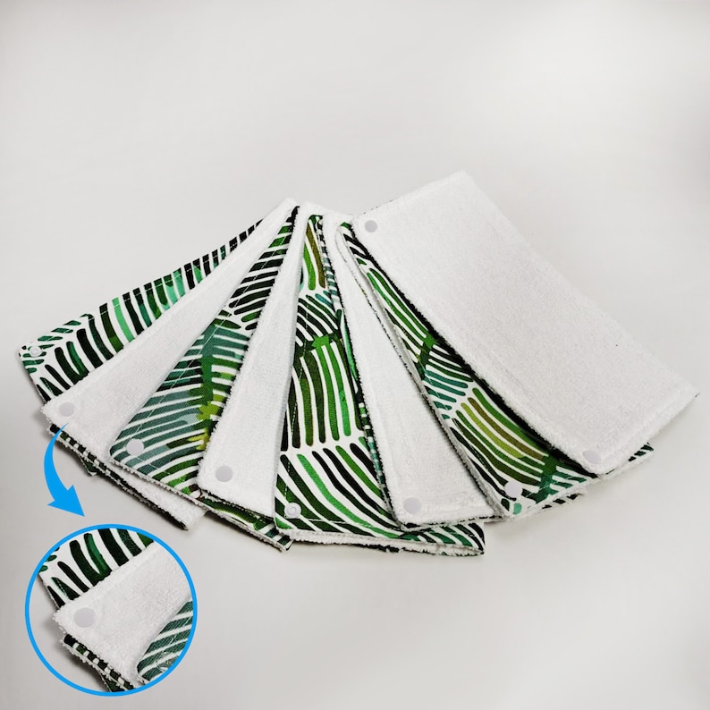 Pu&ograve; includere: Un set di sei bavaglini in tessuto con motivo verde e bianco con bottoni a pressione bianchi. I bavaglini sono piegati a forma di ventaglio.