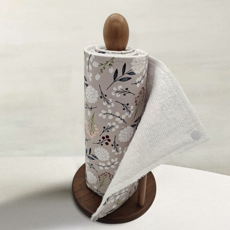 May include: A brown wooden paper towel holder with a white paper towel roll with a floral pattern. The paper towel has a white terry cloth towel attached to it.