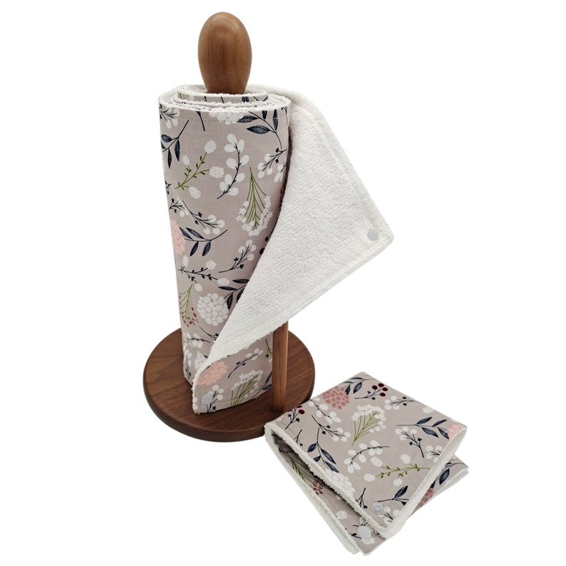 May include: A wooden paper towel holder with a roll of gray and white floral patterned paper towels. Two additional matching cloths are folded and placed on the counter.