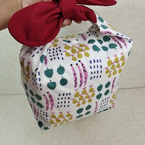 May include: A white fabric tote bag with a red bow on the top. The bag has a colorful geometric pattern with green, pink, yellow, and blue accents.
