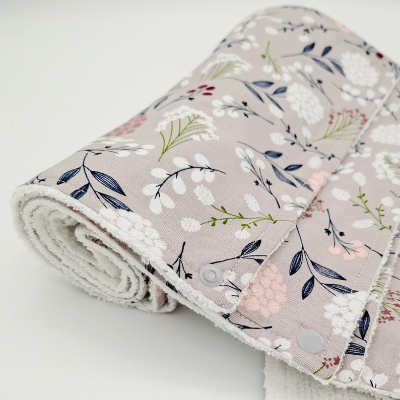 May include: A set of gray fabric burp cloths with a white floral pattern and a white terry cloth backing. The cloths have snaps on the edges.