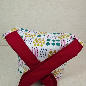 May include: A white fabric headband with a colorful abstract pattern and a red bow tie. The pattern includes green, blue, pink, and yellow shapes.