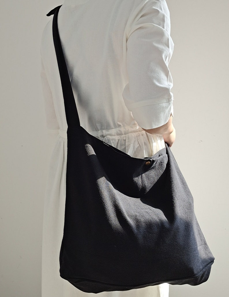 May include: A large black canvas tote bag with a single button closure. The bag is worn over the shoulder and has a long strap.