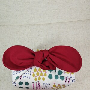May include: A white fabric gift bag with a colorful geometric pattern, tied with a red ribbon bow.