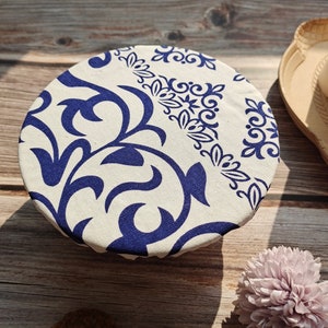May include: A white fabric bowl cover with a blue and white floral pattern. The cover is made of a soft, reusable fabric and is perfect for covering bowls and dishes.
