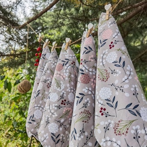 May include: Five tea towels hanging on a clothesline outdoors. The towels are a light gray with a floral pattern in shades of white, pink, and red.