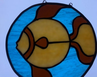 May include: A stained glass window hanging with a brown and yellow fish design on a blue background.