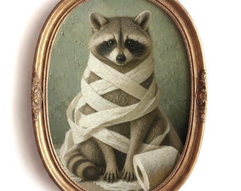 May include: An oval-framed artwork features a raccoon wrapped in white toilet paper. The raccoon has a gray and black face and is seated against a muted green background. The frame is gold with ornate detailing.