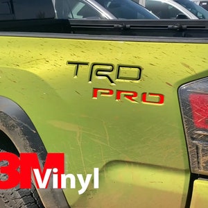 Może przedstawiać: Zielony samochód dostawczy z czarno-czerwonym emblematem "TRD PRO" na boku. Samochód jest pokryty brudem i błotem. Samochód ma naklejkę 3M Vinyl na boku.