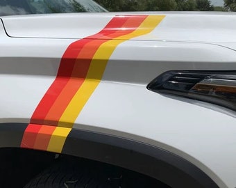 May include: A white truck with a black fender and a red, orange, and yellow stripe decal on the hood.