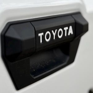 May include: Close-up of a black plastic handle with the word "TOYOTA" in white lettering.