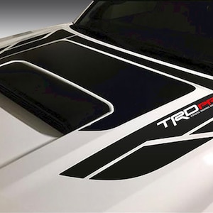 May include: A white car hood with a black and white graphic decal that says "TRD PRO TOYOTA RACING DEVELOPMENT" in red and black letters.