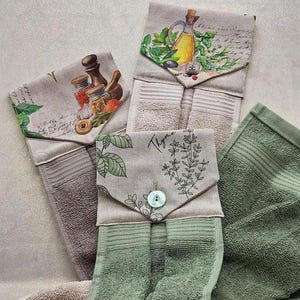 Può includere: Una collezione di strofinacci da cucina con top decorativi. I top presentano disegni botanici e culinari, tra cui olio d'oliva, erbe aromatiche e spezie. Gli asciugamani sono in tonalità di verde, beige e marrone, con chiusure a bottone.
