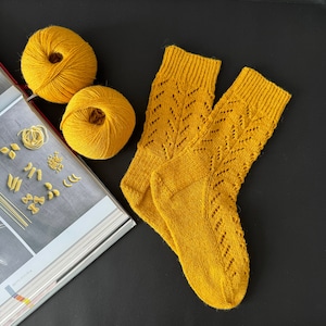 Op de afbeelding: Een paar gele gebreide sokken met een kantpatroon. De sokken zijn gemaakt met een delicate steek en hebben een zacht, comfortabel gevoel.