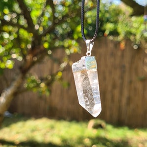 Puede incluir: Un colgante de cristal de cuarzo transparente en un collar de cord&oacute;n negro. El cristal est&aacute; facetado y tiene un engaste de plata.