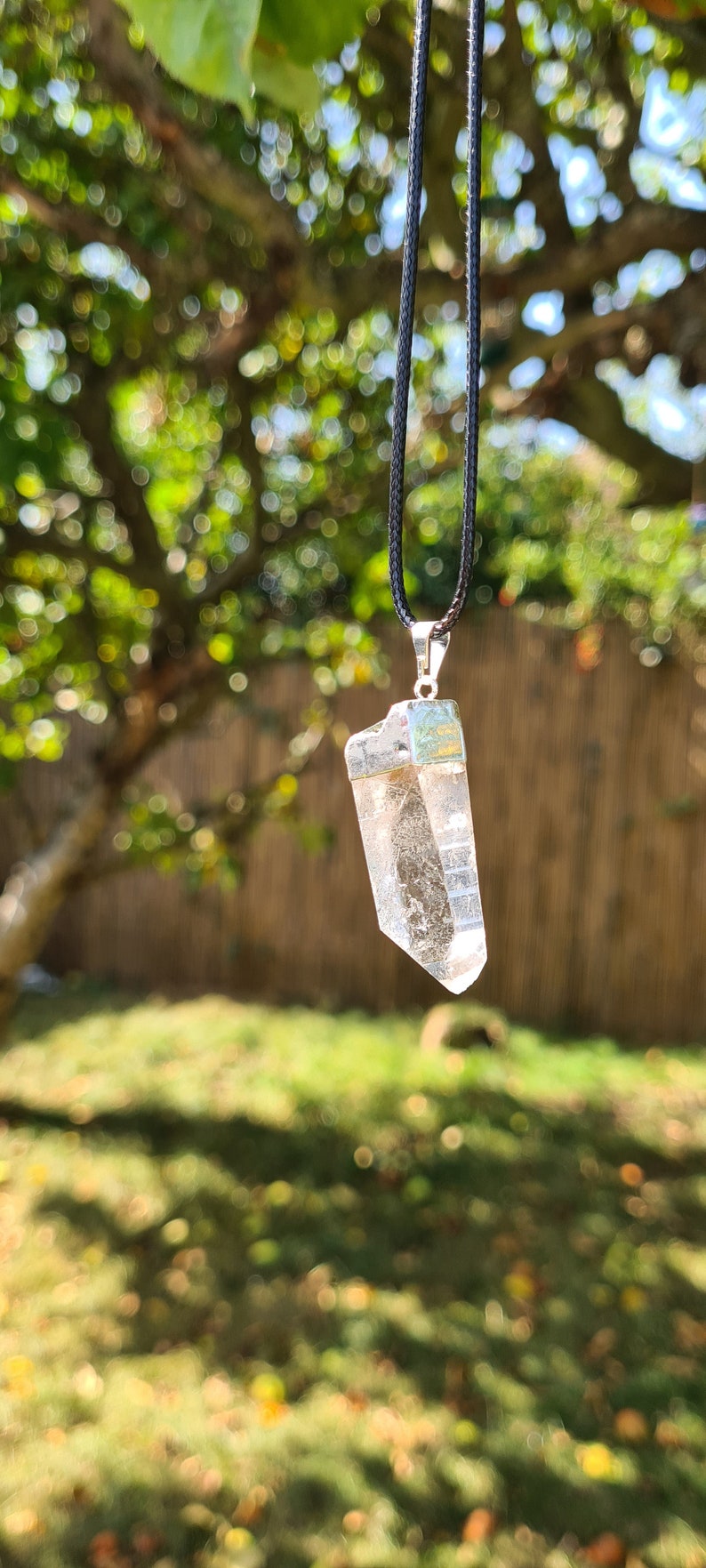 Puede incluir: Un colgante de cristal de cuarzo transparente en un collar de cord&oacute;n negro. El cristal est&aacute; facetado y tiene un engaste de plata.