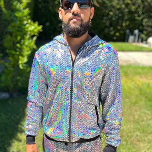 May include: A silver sequined tracksuit with a black zipper and black trim. The jacket has a hood. The pants have a drawstring waist.