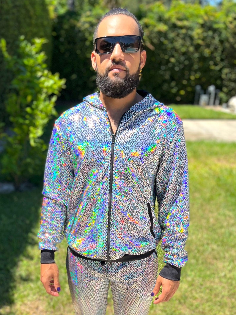 May include: A silver sequined tracksuit with a black zipper and black trim. The jacket has a hood. The pants have a drawstring waist.