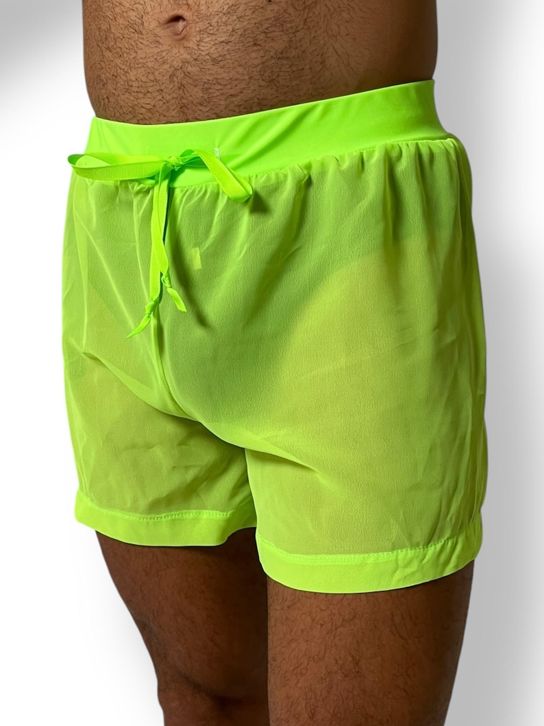 May include: Neon green shorts with a drawstring waist. The shorts are made of a sheer, lightweight fabric. The waistband and hem are a solid neon green.
