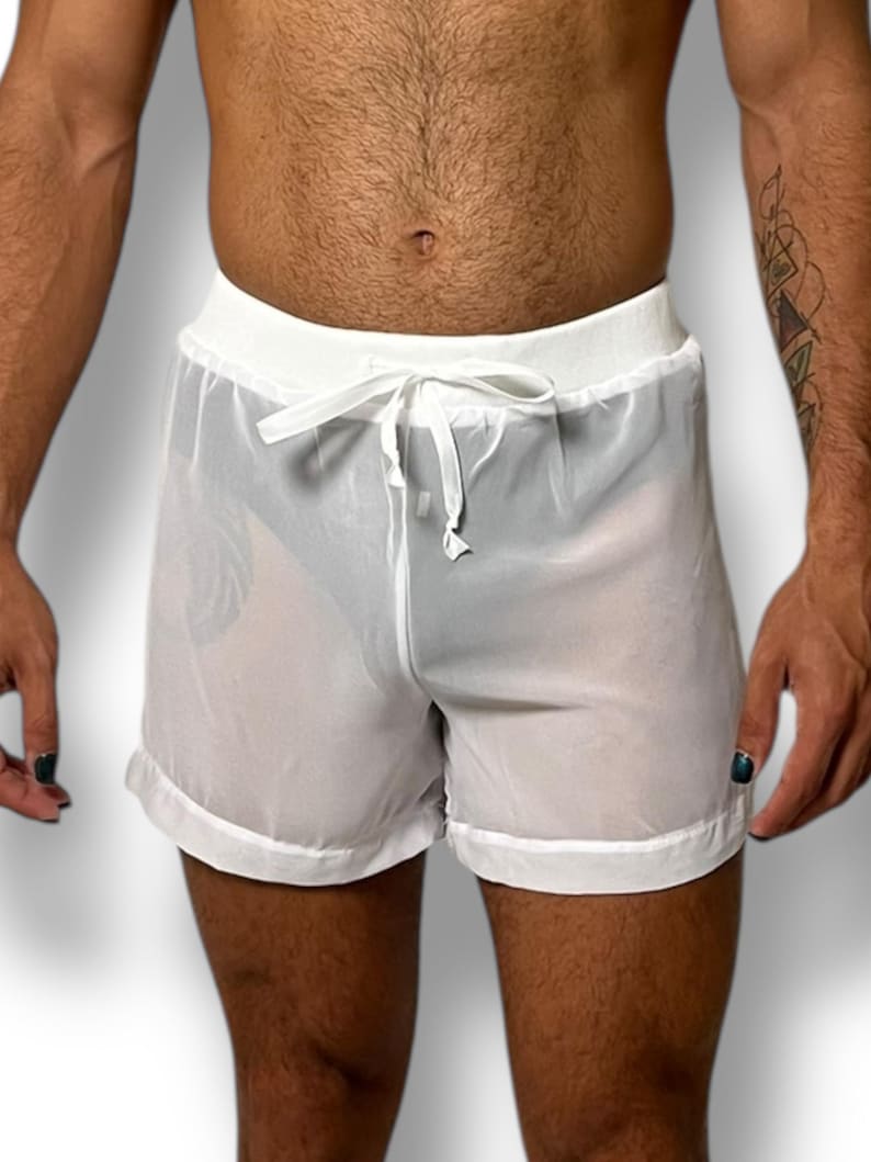 May include: White sheer shorts with a drawstring waist. The shorts have a white trim along the bottom hem and waistband. The fabric is lightweight and slightly transparent.