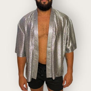 May include: A metallic silver open-front kimono-style shirt with short sleeves and a textured, shimmering finish. The garment features a wide, structured collar band and a loose, boxy fit, crafted from a lightweight, reflective fabric material.