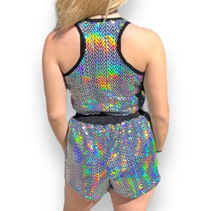May include: A silver iridescent sequined tank top and matching shorts. The tank top has a black racerback design. The shorts have a black elastic waistband.