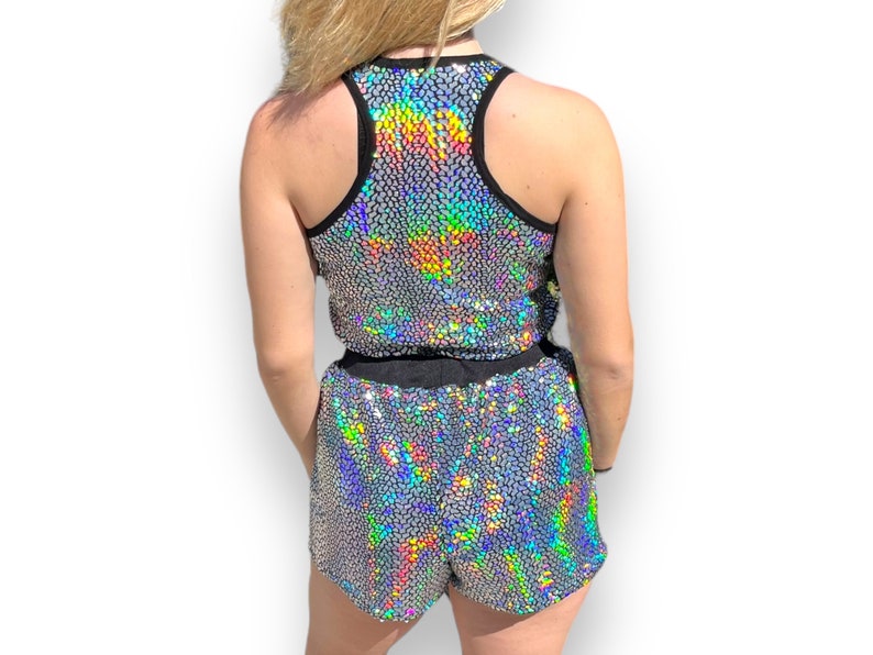 May include: A silver iridescent sequined tank top and matching shorts. The tank top has a black racerback design. The shorts have a black elastic waistband.