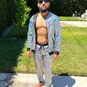 May include: A silver sequined tracksuit with a black zipper and drawstring. The jacket has a hood. The pants have a drawstring waist. The person is wearing sunglasses.