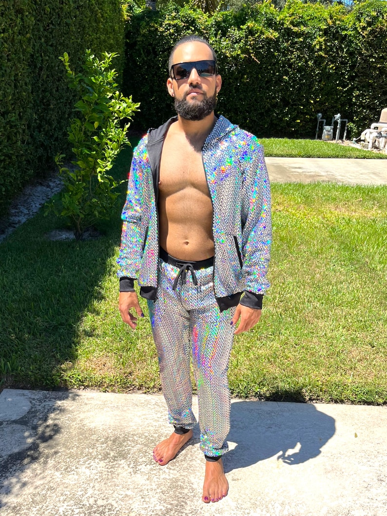 May include: A silver sequined tracksuit with a black zipper and drawstring. The jacket has a hood. The pants have a drawstring waist. The person is wearing sunglasses.