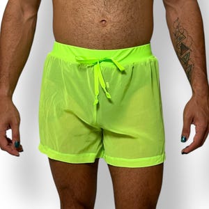 May include: Neon green mesh shorts with a drawstring waist. The shorts are made of a lightweight, sheer fabric. The shorts have a relaxed fit and are suitable for swimwear or casual wear.