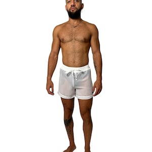 May include: White, semi-sheer shorts with a drawstring waist. The shorts have a simple, minimalist design, perfect for swimwear or casual wear. The shorts are shown on a person.