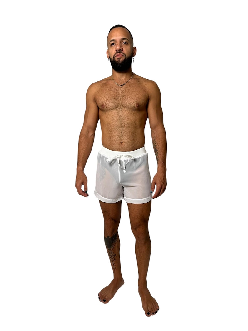 May include: White, semi-sheer shorts with a drawstring waist. The shorts have a simple, minimalist design, perfect for swimwear or casual wear. The shorts are shown on a person.