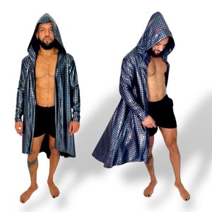 Op de afbeelding: Een lange jas met capuchon en lange mouwen in een zilver-zwart stippenpatroon. De jas heeft een zwarte binnenkant en is aan de voorkant open. Het model draagt een zwarte korte broek. Een uniek mode-item.